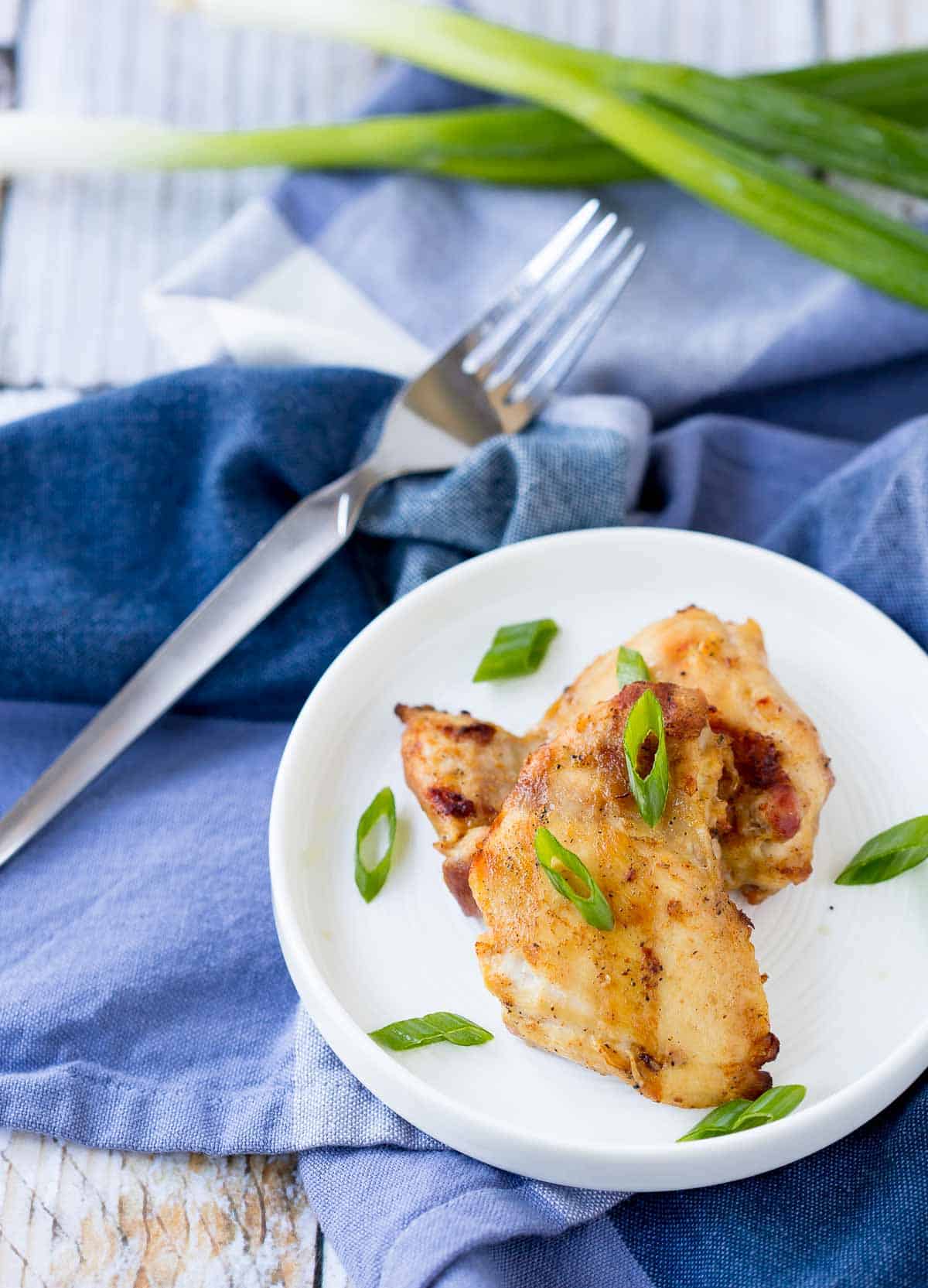 Overhead of grilled chicken on small white plate, garnished with sliced green onions.