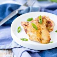 Grilled chicken on small white plate, garnished with sliced green onions.