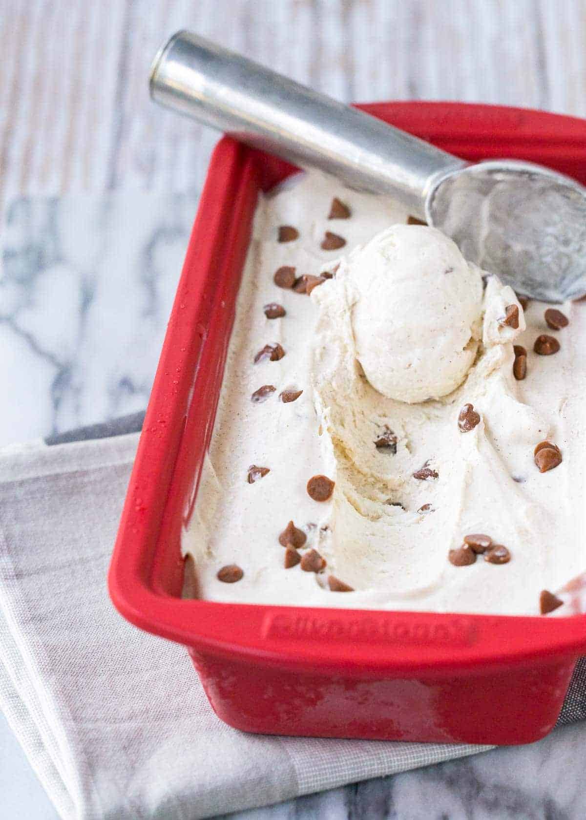 Frozen ice cream in red ceramic loaf pan, with ice cream scoop.