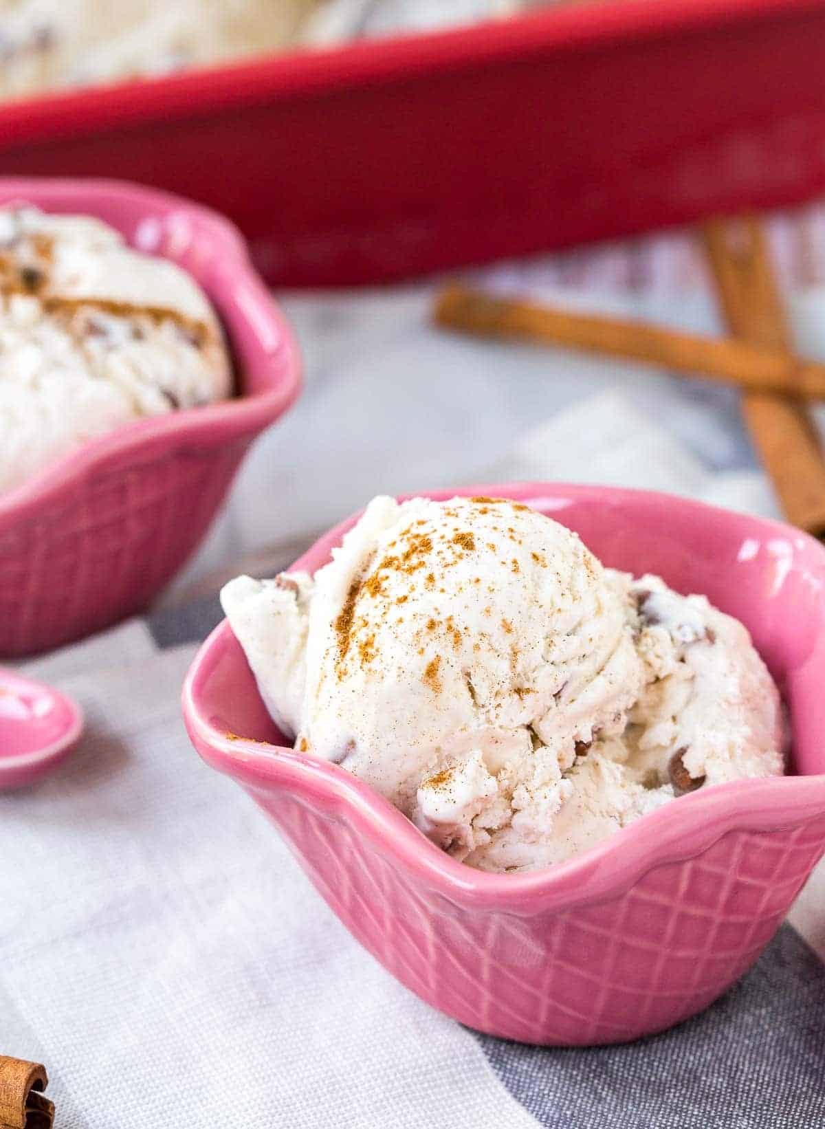 Decorative pink bowls with cinnamon ice cream, with cinnamon sticks scattered around bowls.