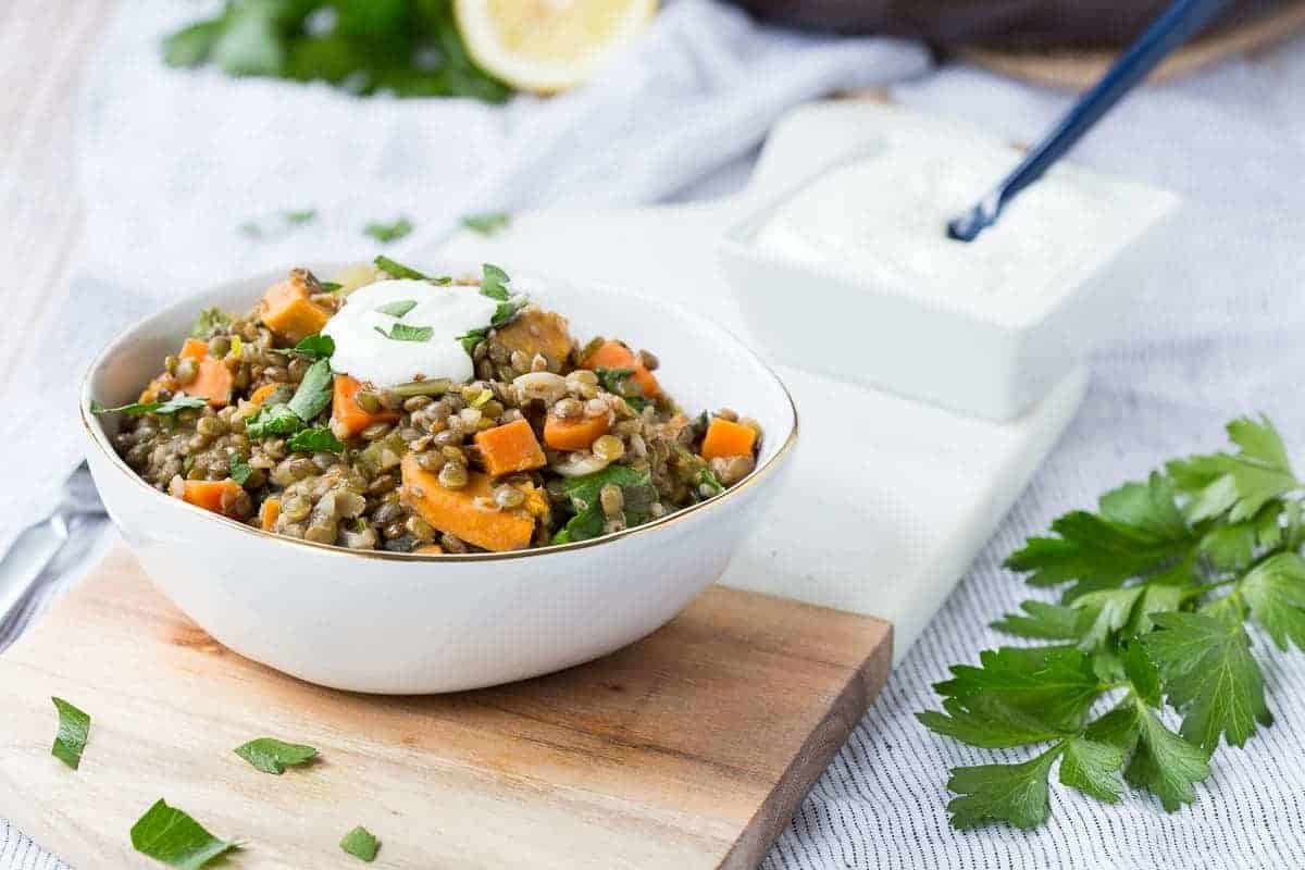 Front view of a serving of one pot lentils in serving bowl with bowl of yogurt in background.