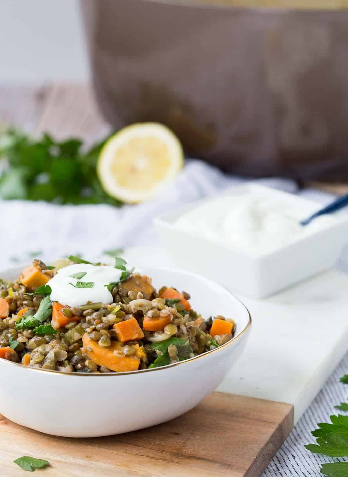White decorative bowl containing hearty lentil stew, garnished with cilantro and Greek yogurt.