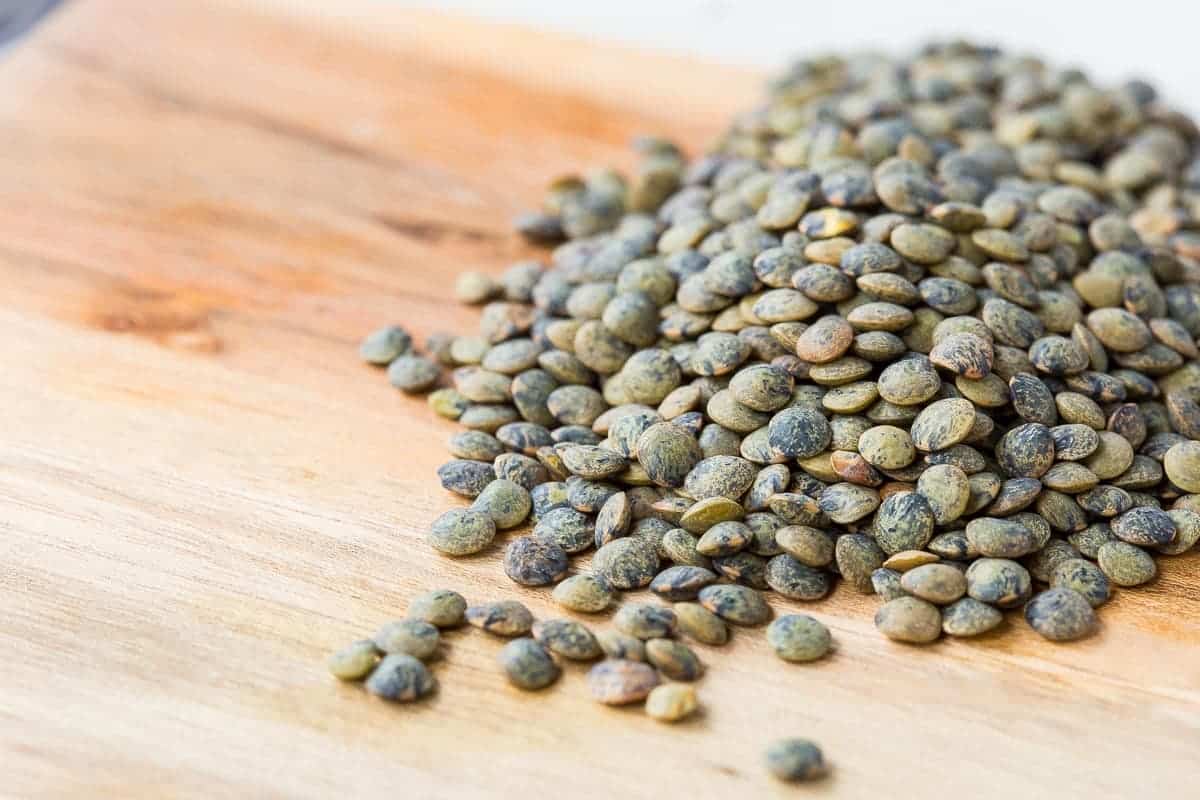 Uncooked French green lentils spilled out onto wooden cutting board.