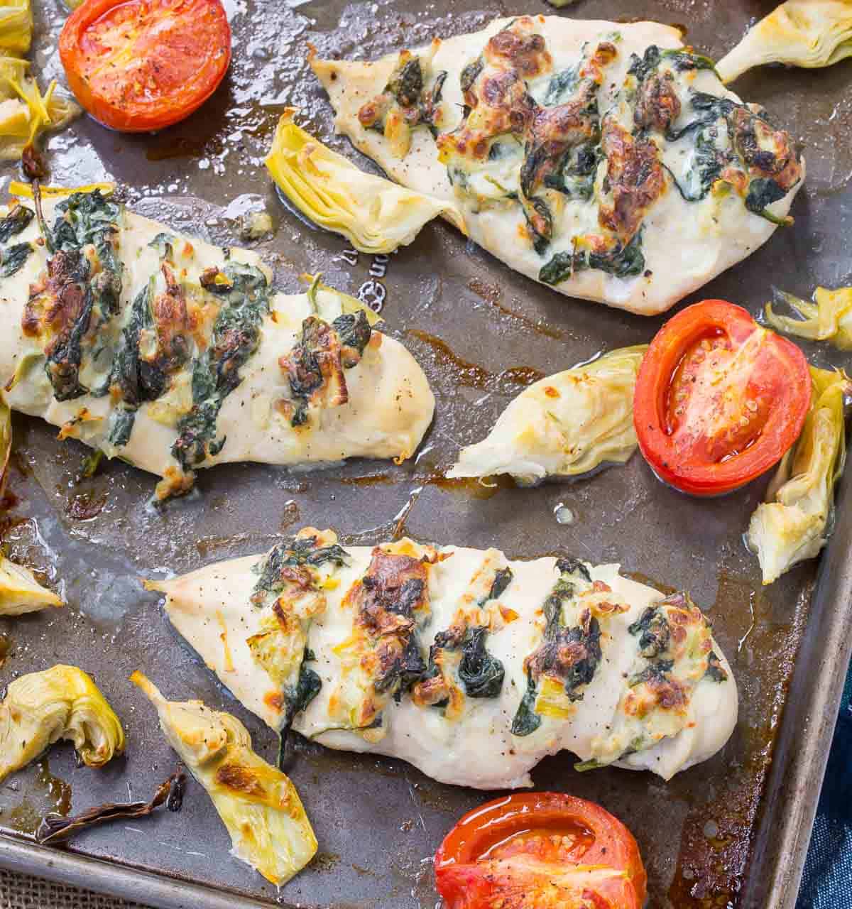 Overhead of stuffed chicken on sheet pan with tomatoes and artichoke hearts.