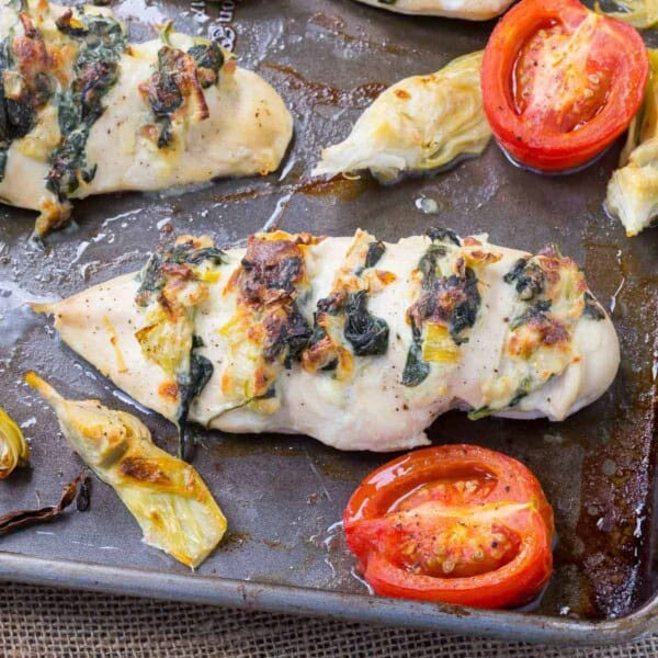 Overhead of stuffed chicken, halved tomatoes, and artichoke hearts in sheet pan.