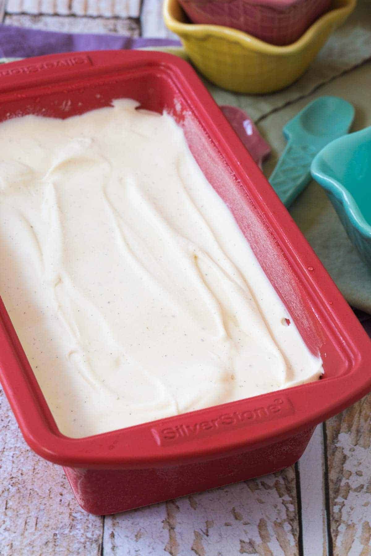 A red loaf pan full of vanilla bean ice cream.