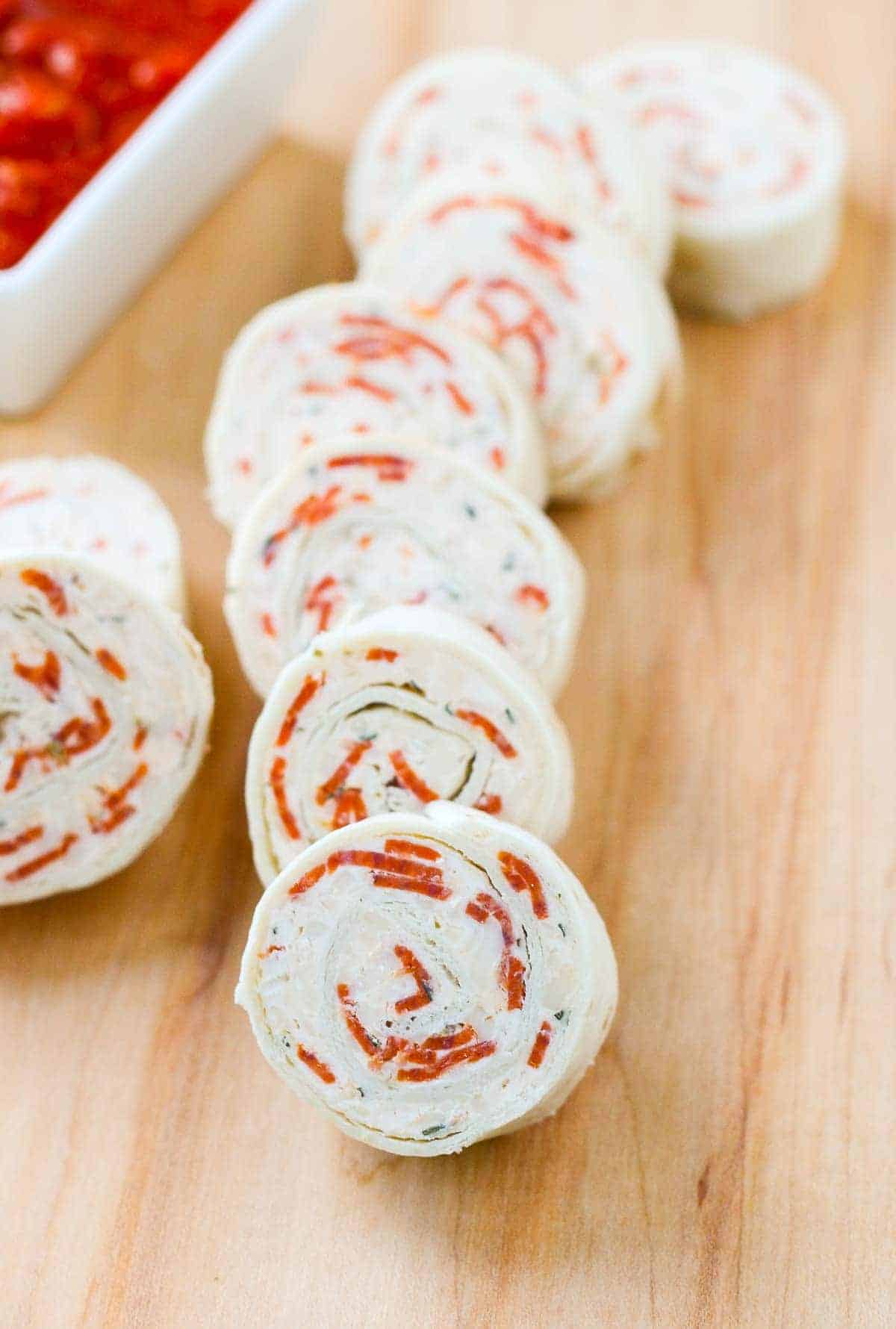 Pizza tortilla pinewheels arranged on a wooden board.