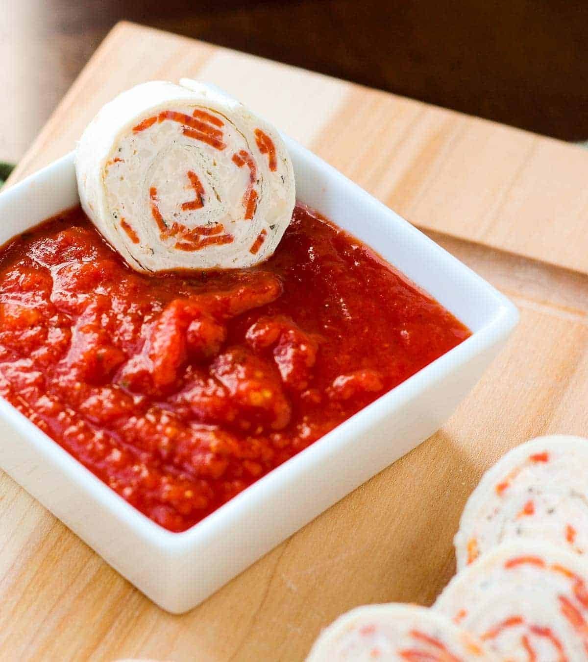 Pizza tortilla pinwheel being dipped in pizza sauce.