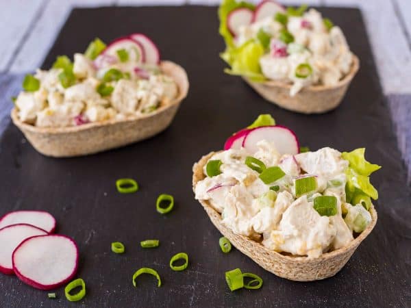Three tortilla boats filled with chicken salad, garnished with sliced radishes and green onions.