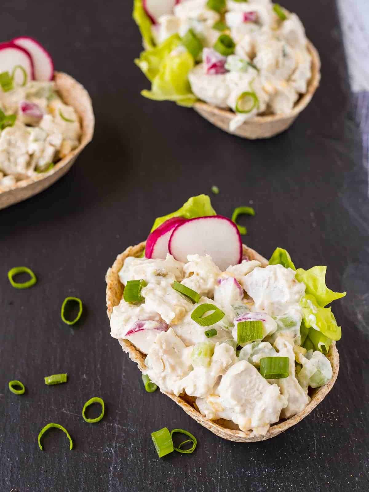 Chicken salad in tortilla boats garnished with sliced green onions.
