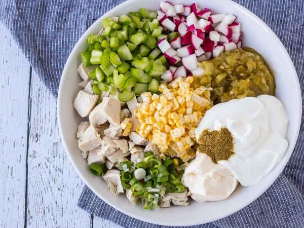 Overhead of green chile chicken salad ingredients in shallow white bowl.