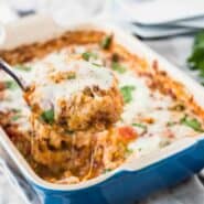 Baked casserole in blue baking dish, with spoon lifting out a serving.