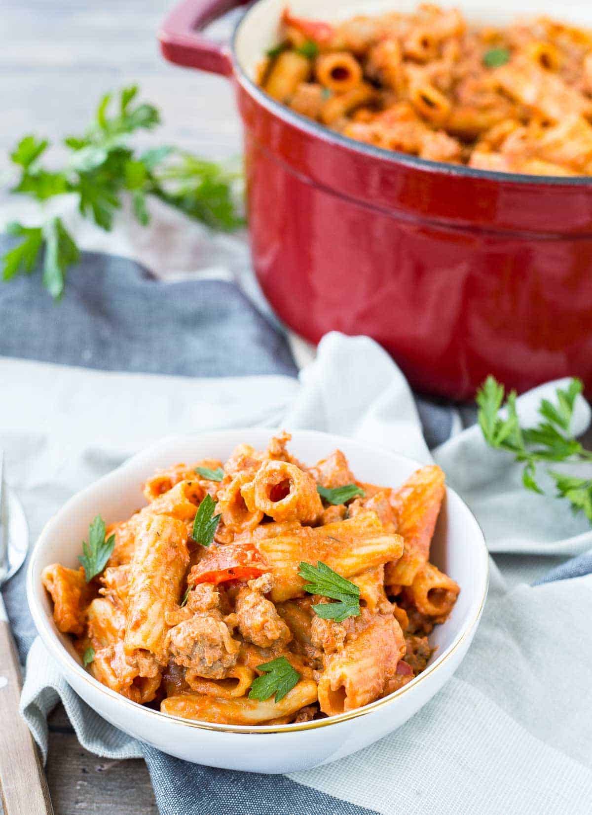 Small bowl of pasta garnished with fresh parsley with red Dutch oven in background.