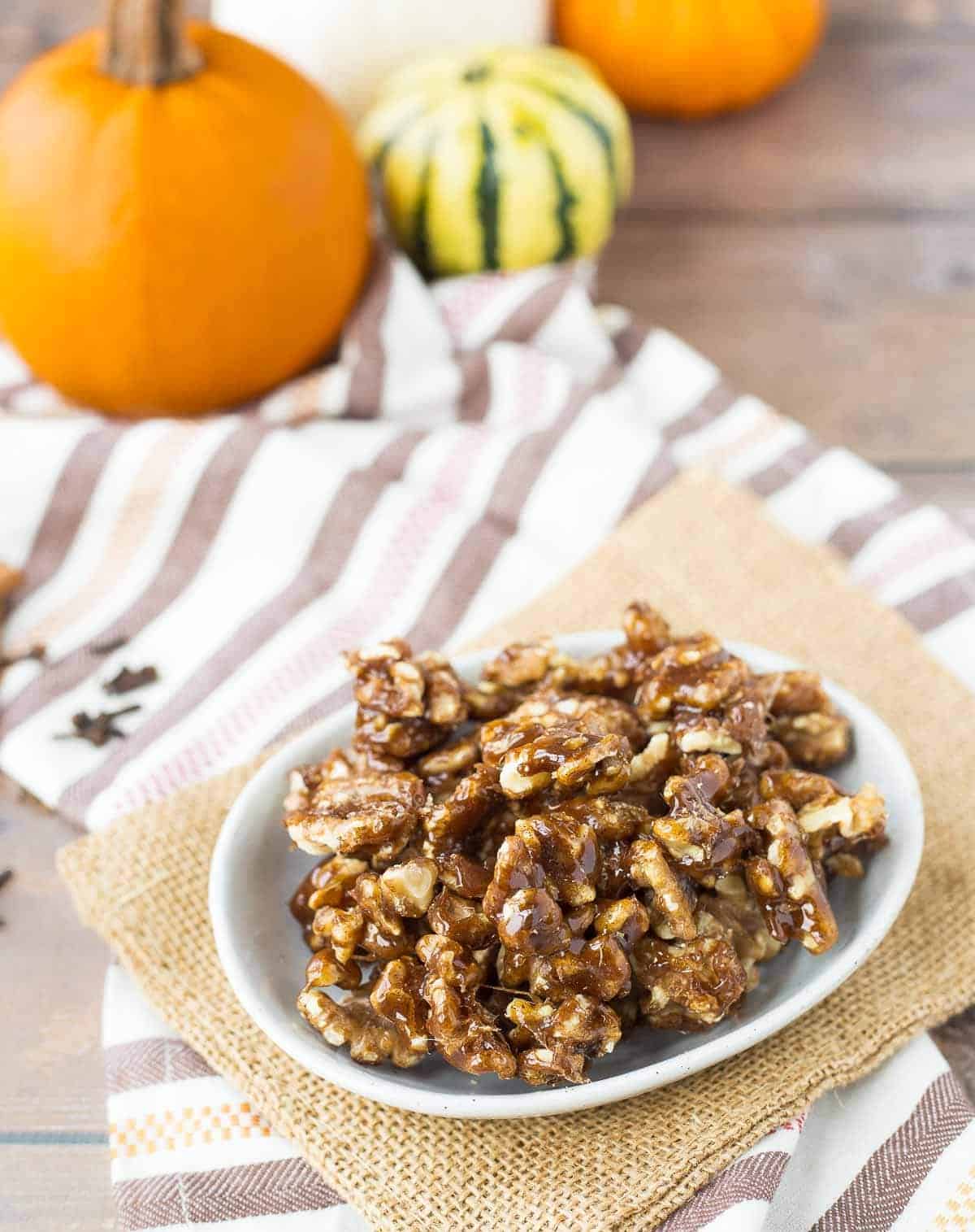 A bowl of pumpkin spice candied walnuts on a table with orange pumpkins in the background.