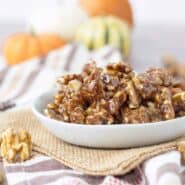 A bowl of pumpkin spice candied walnuts on a table with orange pumpkins in the background.