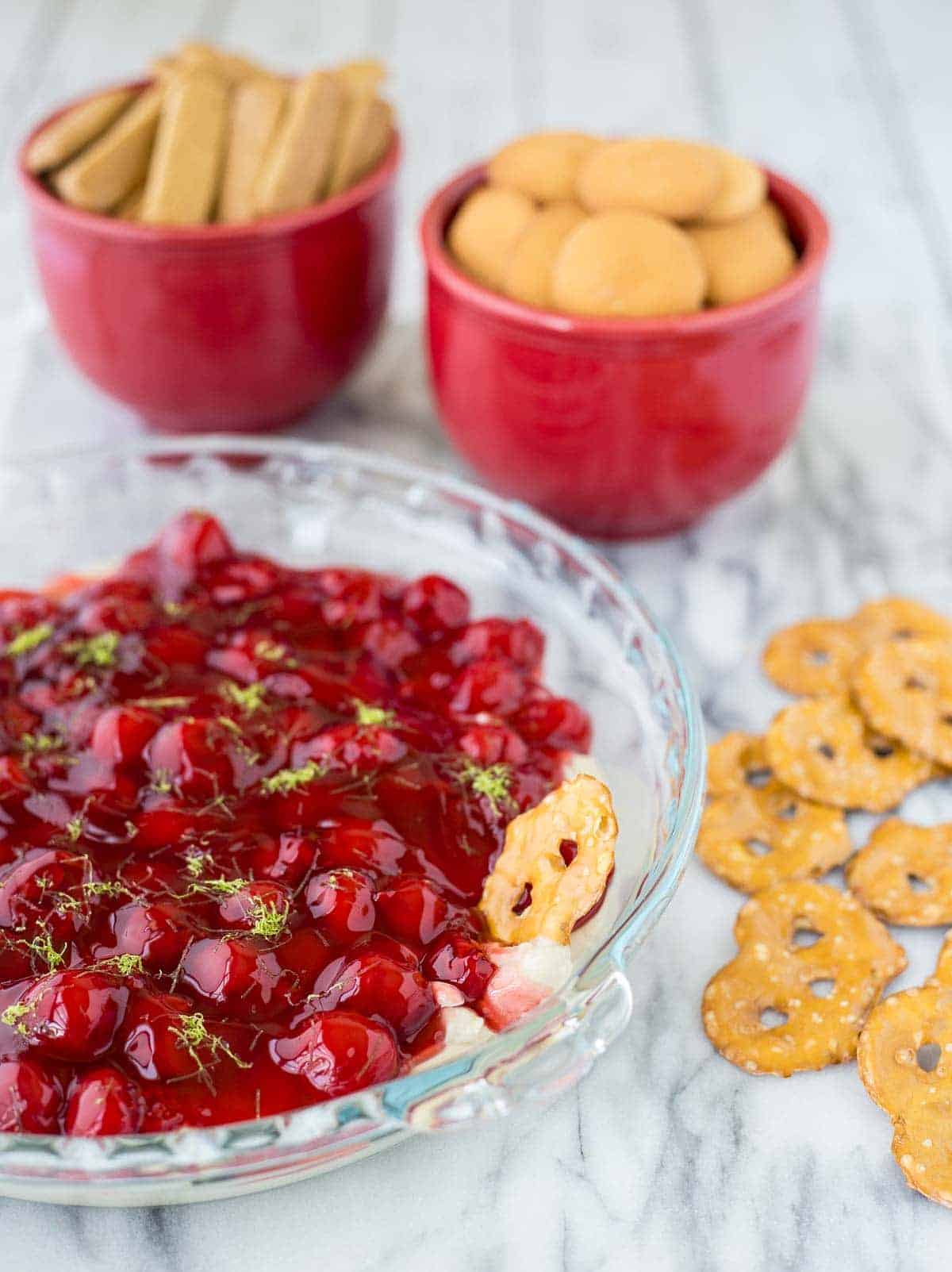 Pretzel being dipped in cherry cheesecake dip.