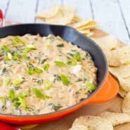 Mexican spinach dip in orange cast iron skillet surrounded by tortilla chips.