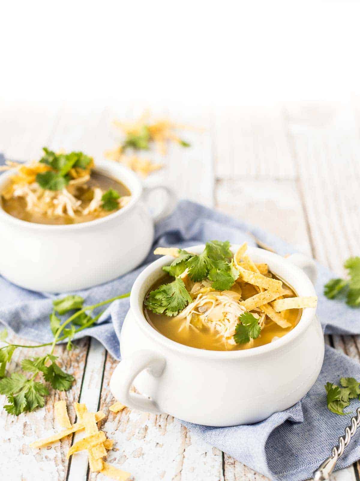 Chicken enchilada soup in white soup bowls with handles.