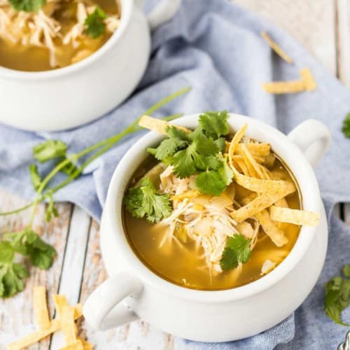 Overhead of white soup bowls containing chicken enchilada soup with garnishes.