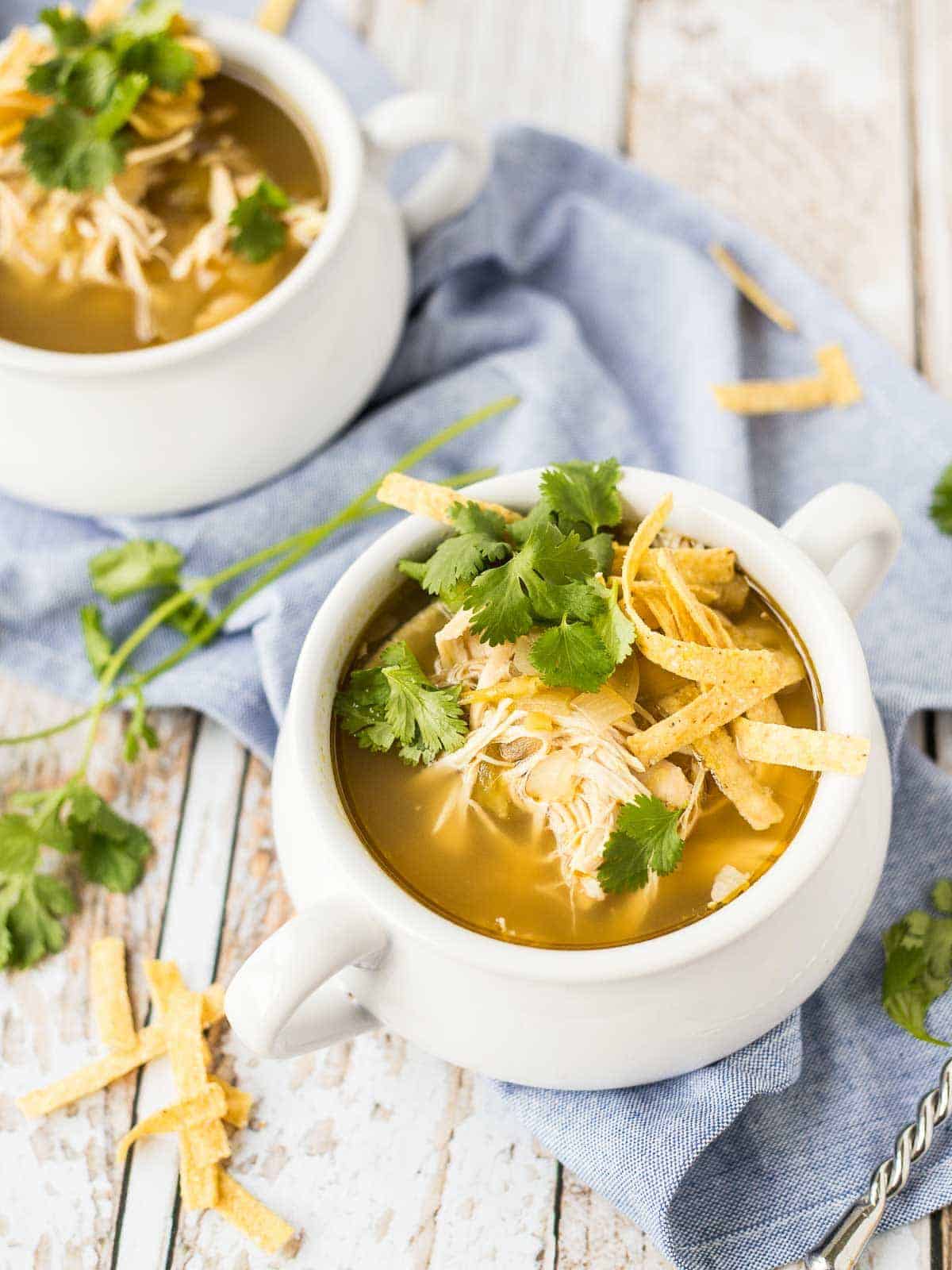 Overhead of soup in bowls, garnished with cilantro leaves, shredded cheese, and tortilla strips.