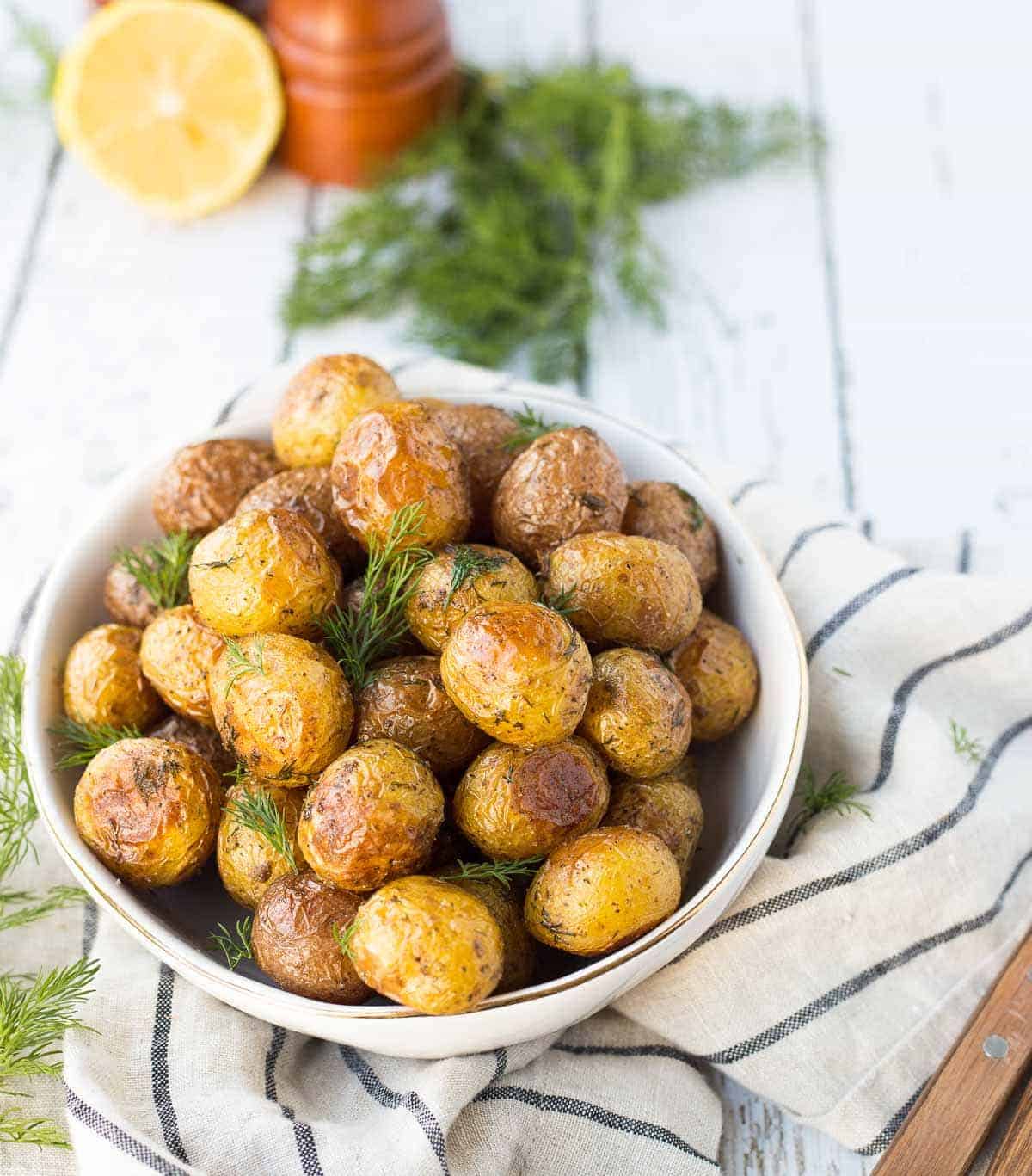 Overhead of roasted potatoes in serving bowl, garnished with fresh dill.