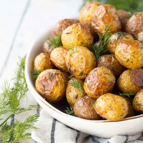 Partial image of roasted potatoes in round white serving dish, garnished with fresh dill.