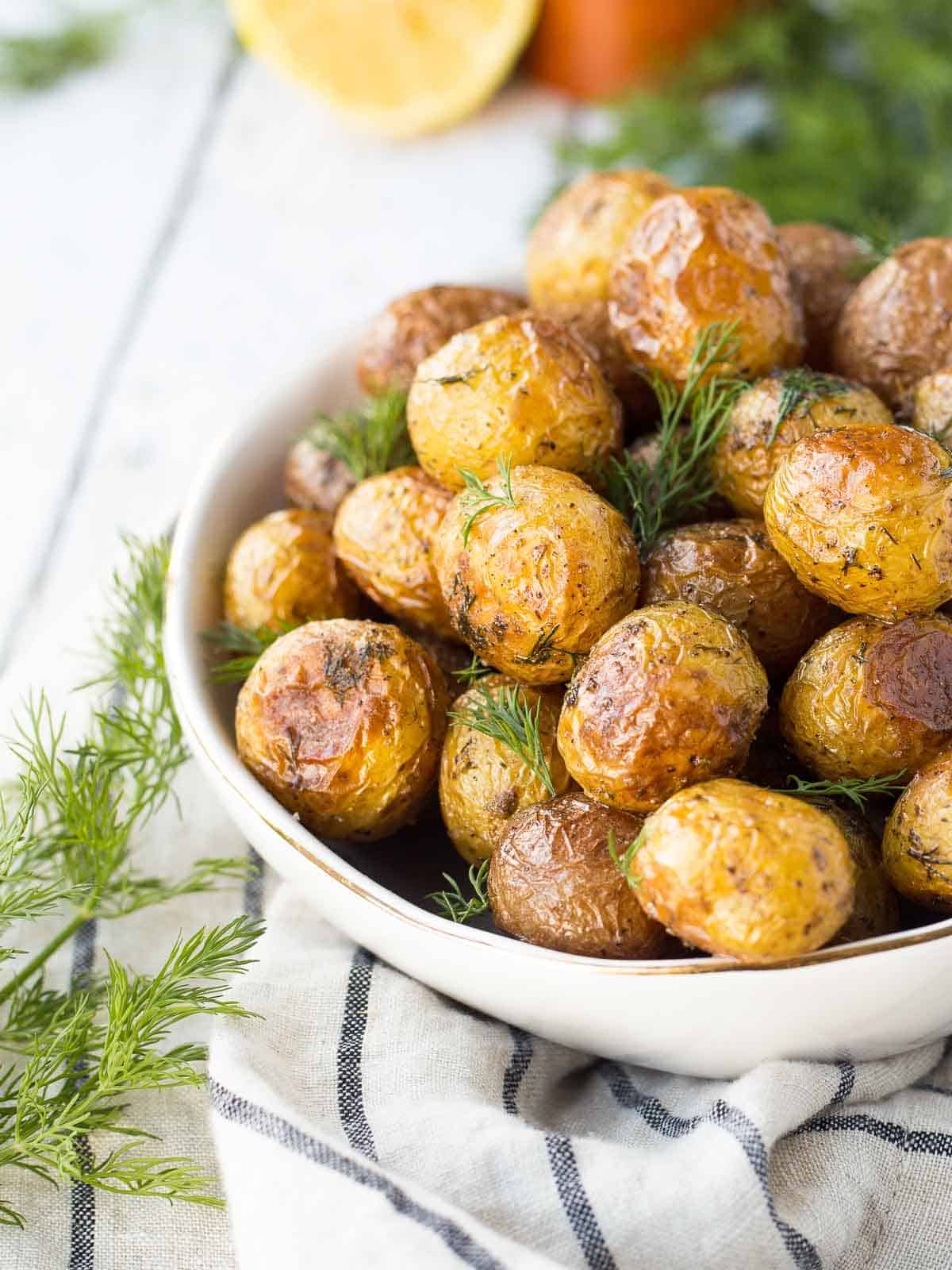 Partial front view of roasted potatoes in round white bowl, garnished with fresh dill.