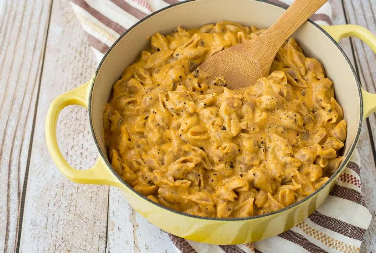 Pumpkin mac and cheese in a yellow pot with a wooden spoon.