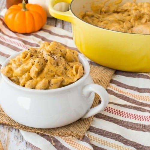 close view of pumpkin macaroni and cheese beer in white bowl with wooden spoon and a yellow crockpot in the background