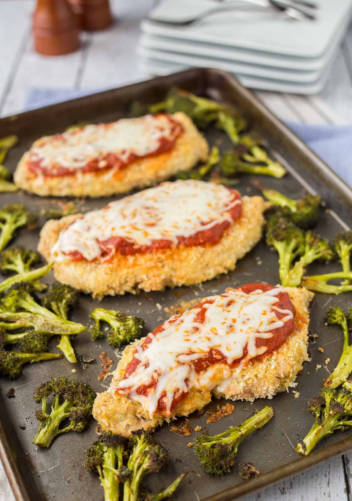 Three chicken breasts on sheet pan with broccoli.