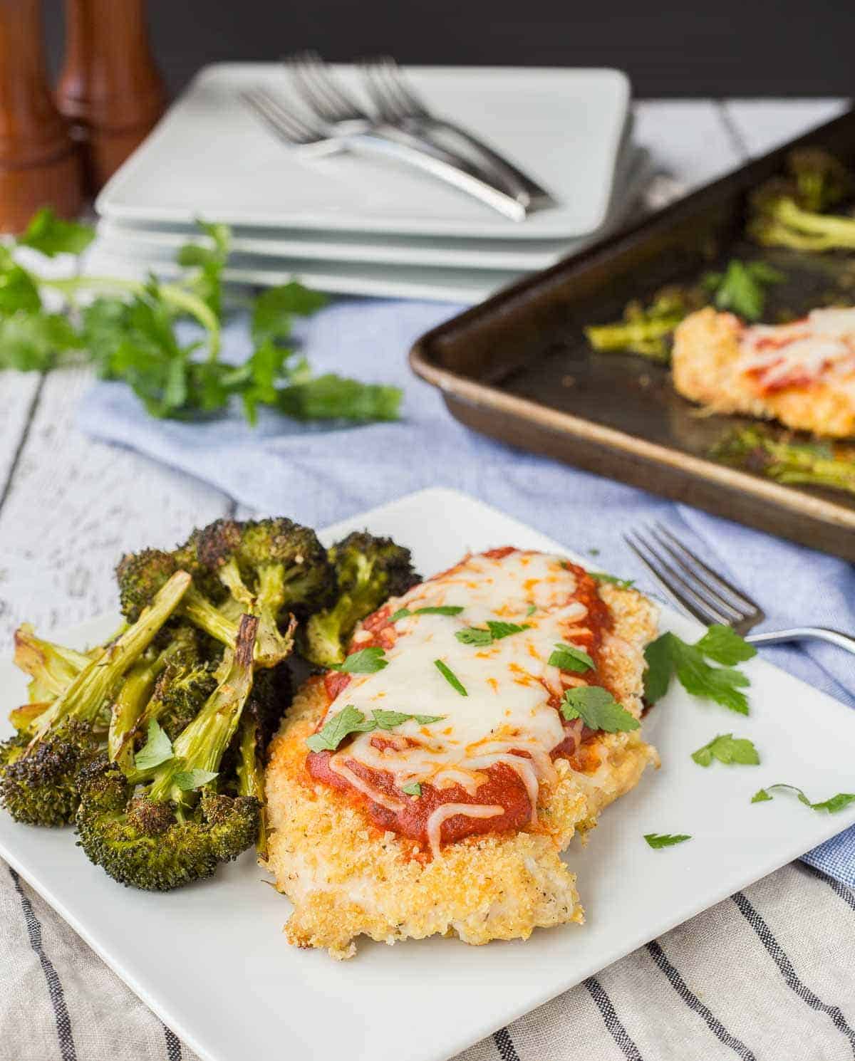 One serving of chicken Parmesan and broccoli on square white plate with fork.