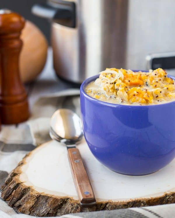 Front view of soup in blue mug with spoon on wood slice.