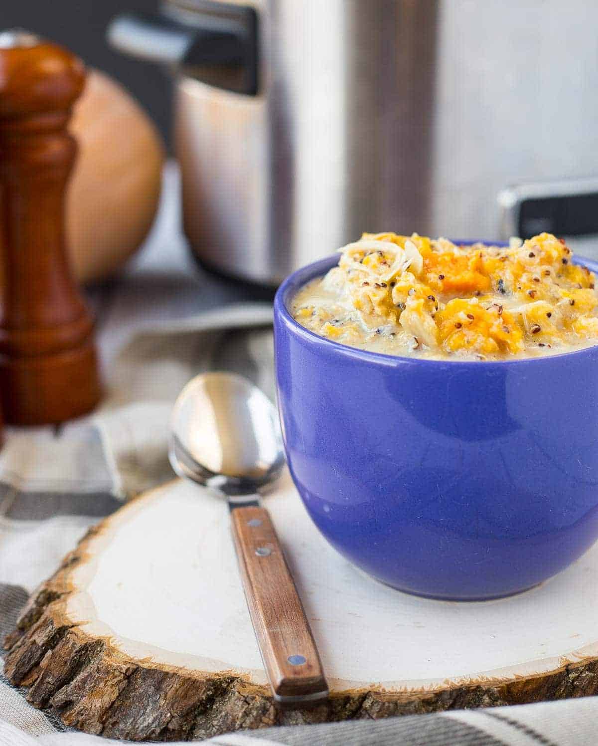 Front view of soup in blue mug with spoon on wood slice.