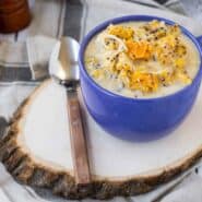 Chicken soup in blue mug with spoon on wood slice.