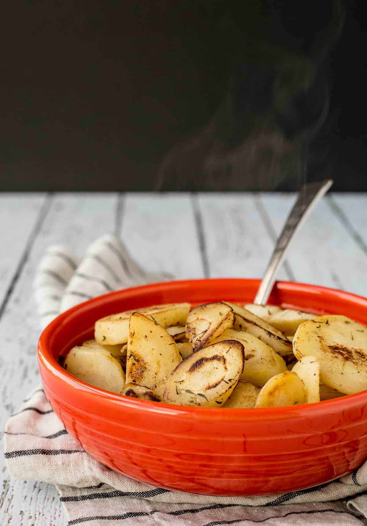 Orange serving dish with parsnips and spoon.