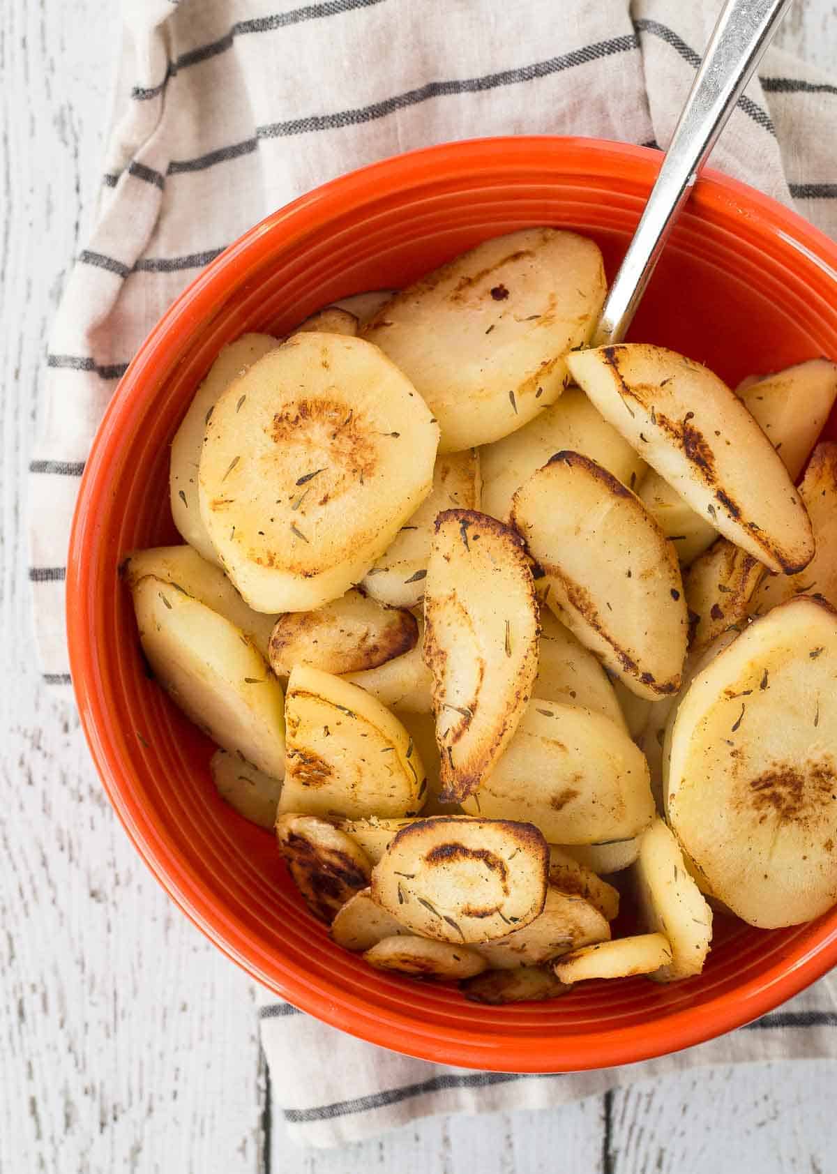 Orange serving dish with sautéed parsnips and spoon.