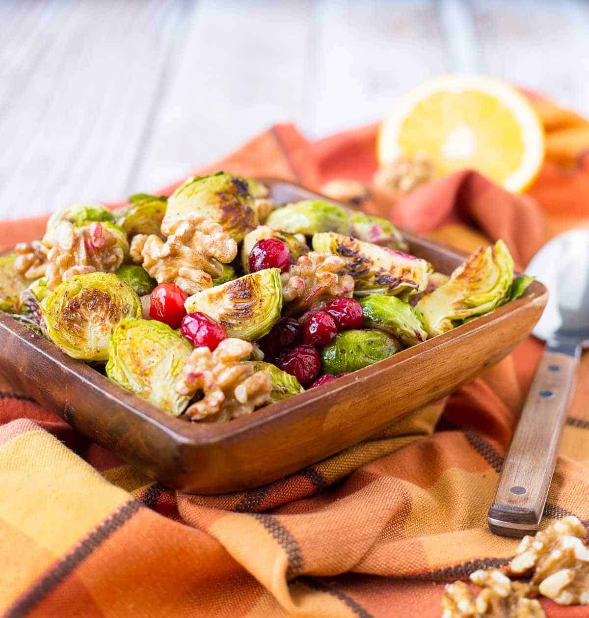 Front view of wooden square bowl containing roasted brussels sprouts.