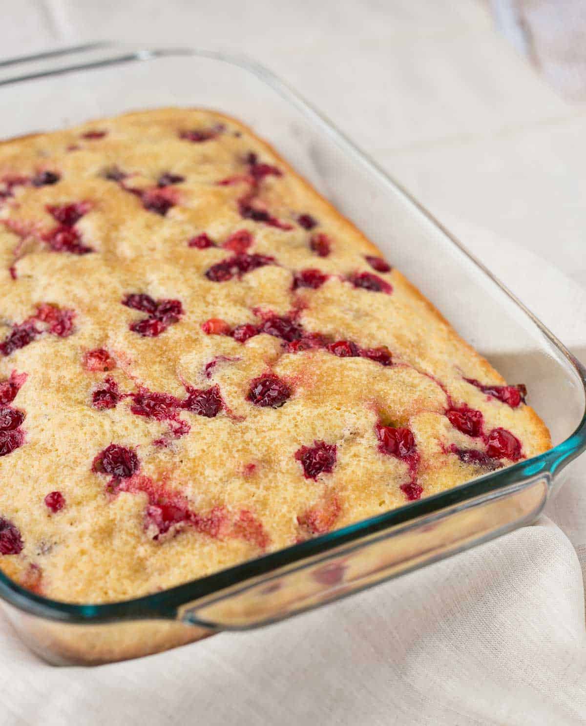 Partial overhead of cake in clear glass baking dish, on white cloth background.