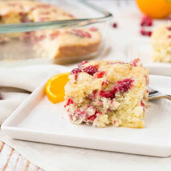 A serving of cranberry coffee cake on a square white plate with baking pan in background.