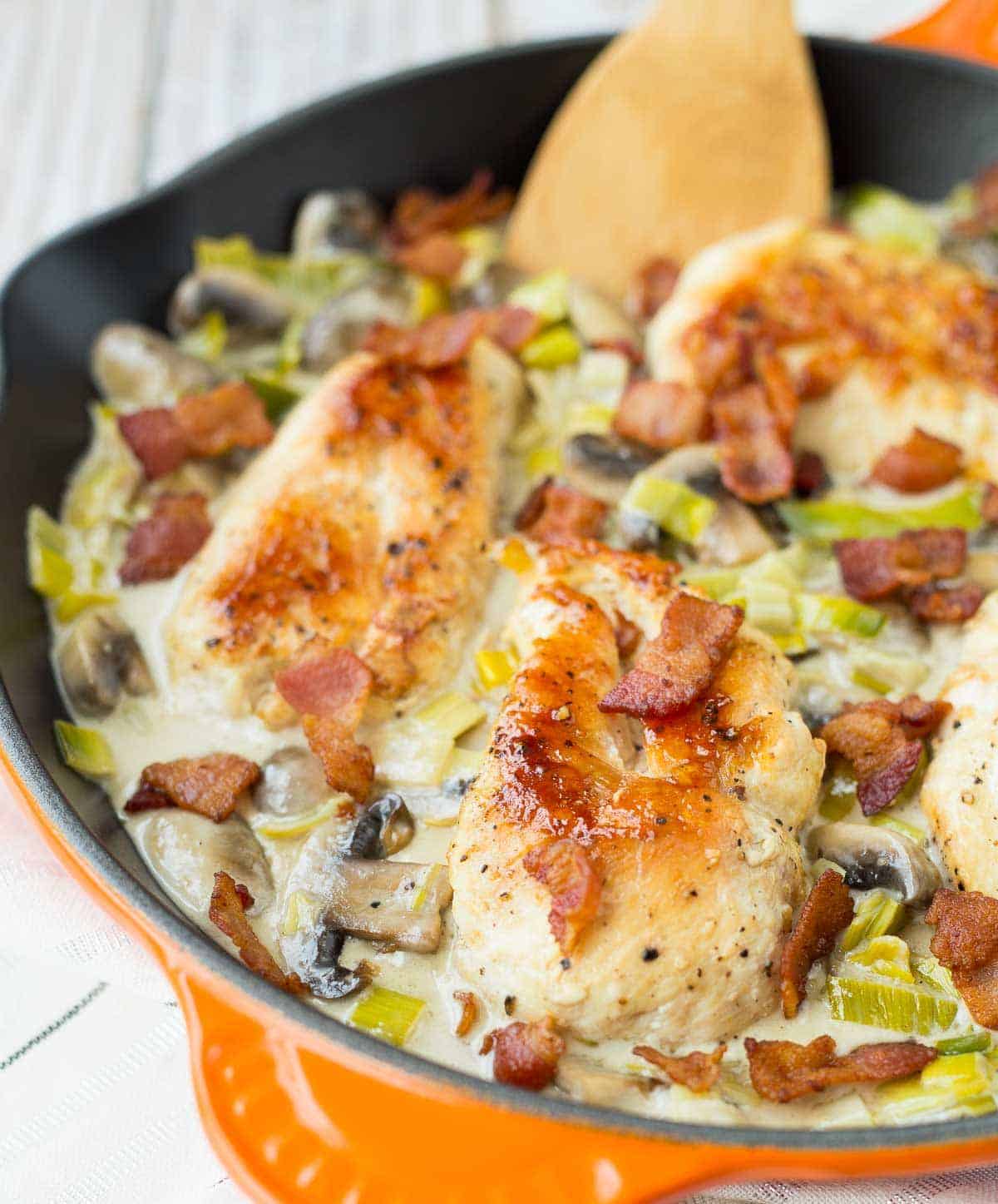 Chicken in orange cast iron skillet with wooden spoon inserted.