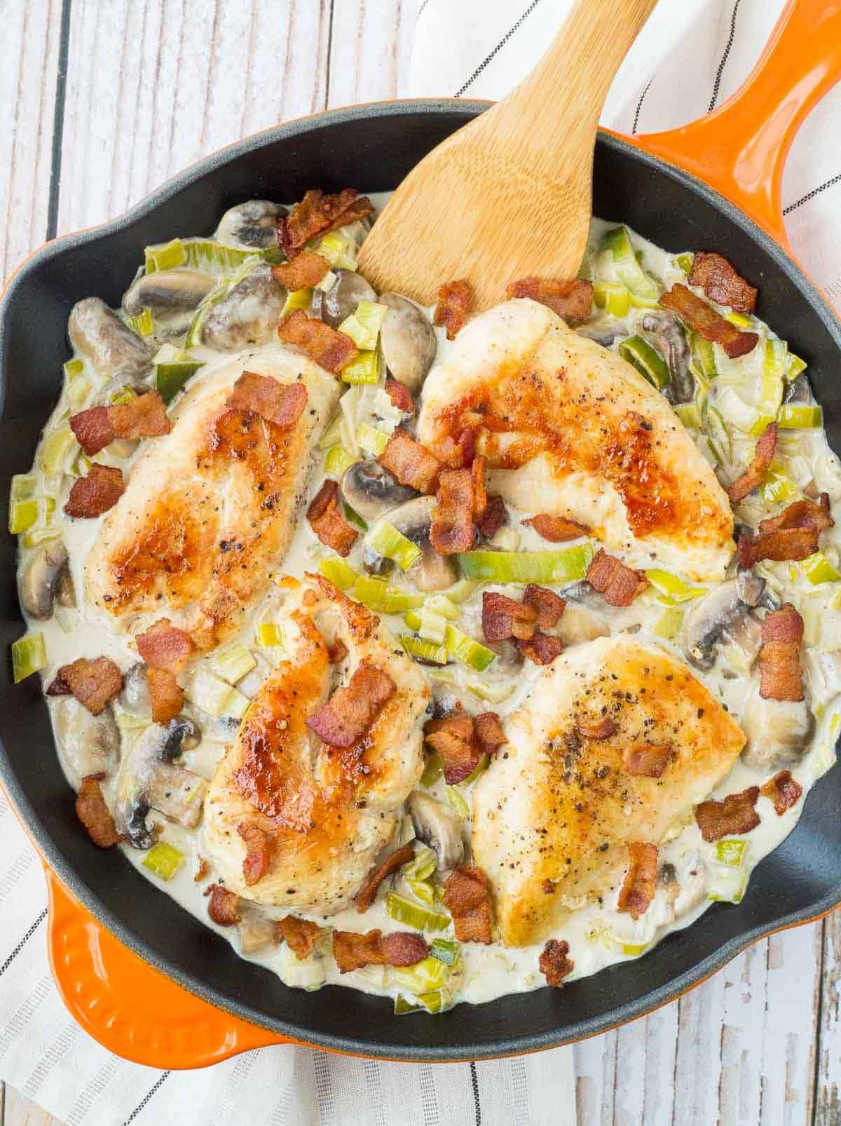 image of white wine chicken in orange skillet with bacon, leeks and mushrooms