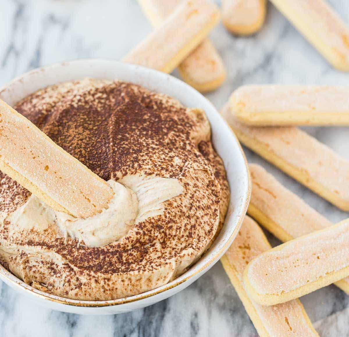 Closeup of dip in decorative bowl, shown with a ladyfinger scooping out dip.