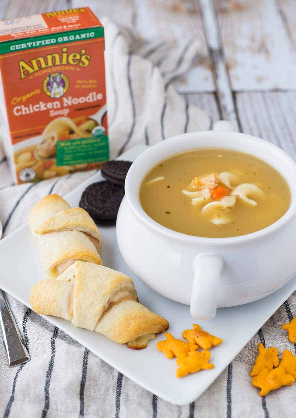 Crescent roll sandwiches on square plate with bowl of soup, bunny crackers, and oreo cookies.