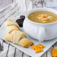 Sandwiches, crackers, bowl of soup, and cookies on square white plate.