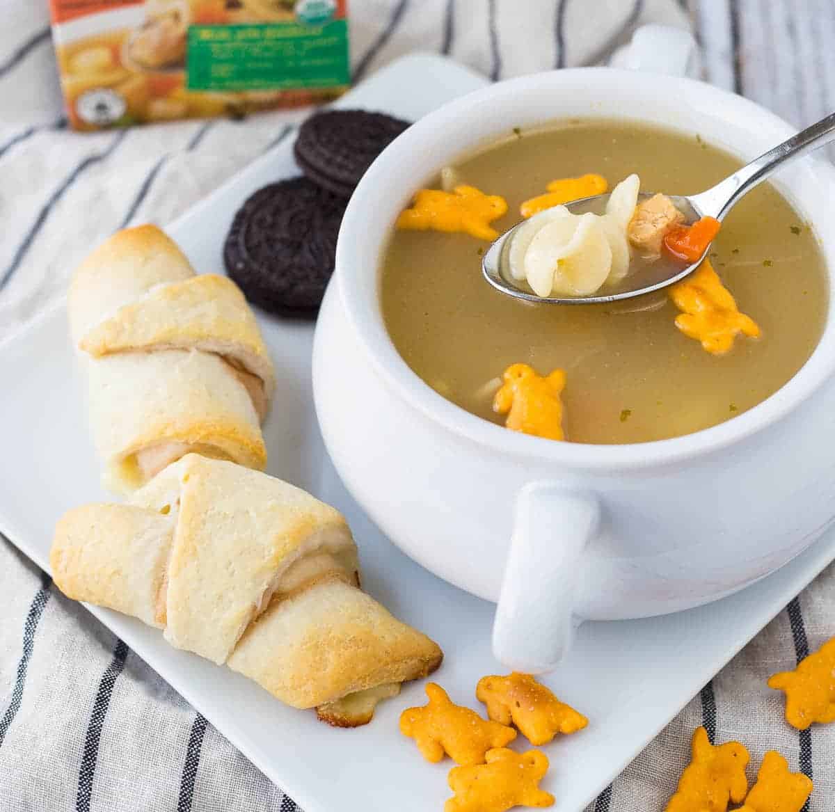 Sandwiches, soup, crackers, and cookies on square white plate.