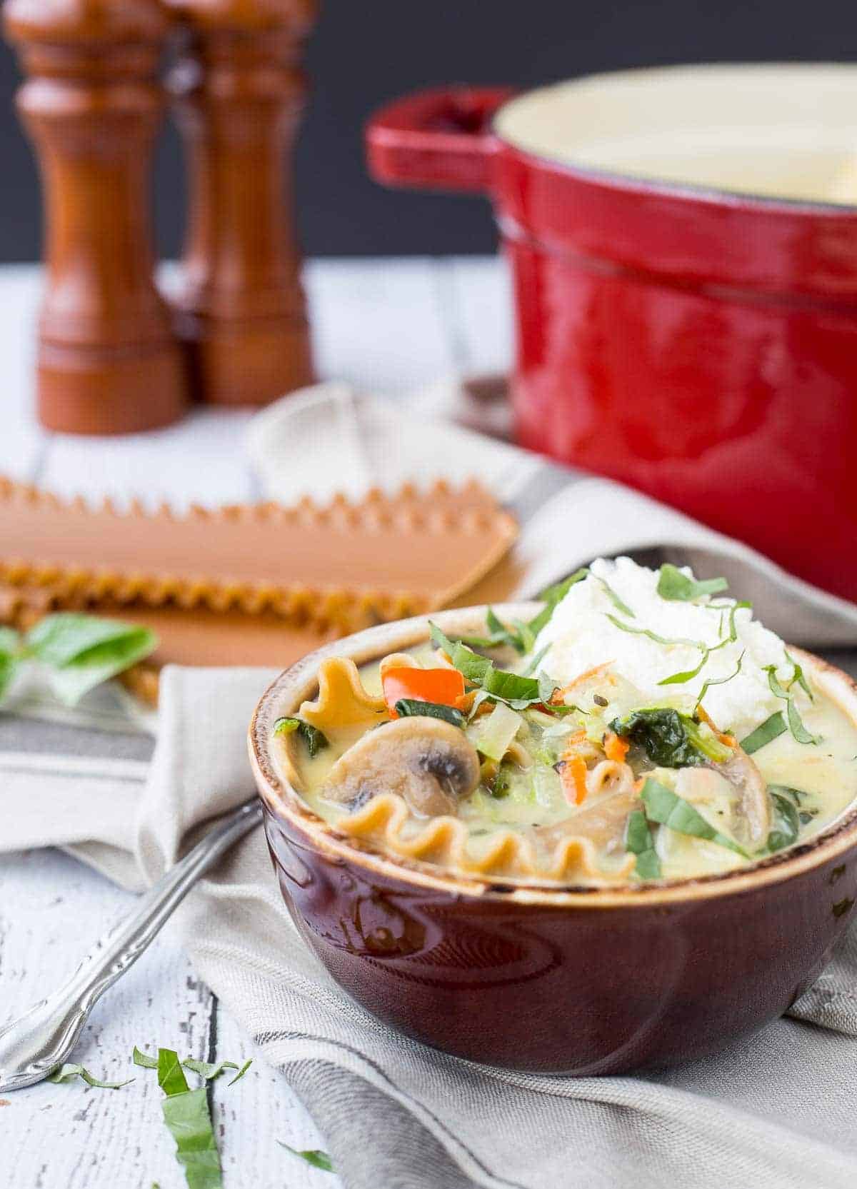 Serving of soup in brown earthern ware bowl, garnished with ricotta cheese and fresh basil.