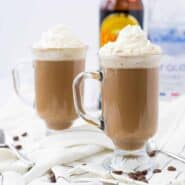 Front view of two clear glass footed mugs containing White Russian hot chocolate garnished with whipped cream.