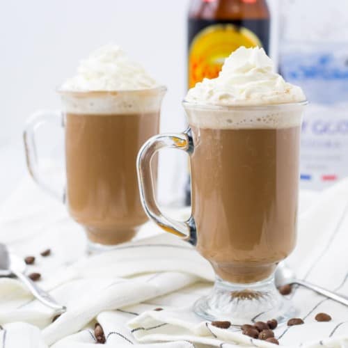 Front view of two clear glass footed mugs containing White Russian hot chocolate garnished with whipped cream.