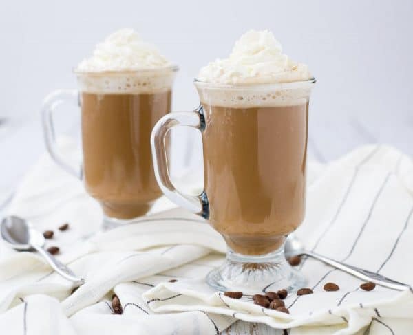 Front view of two mugs of white Russian hot chocolate with two spoons on cloth. 
