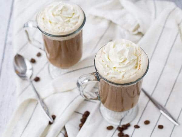 Overhead of two mugs of white russian on white striped cloth.